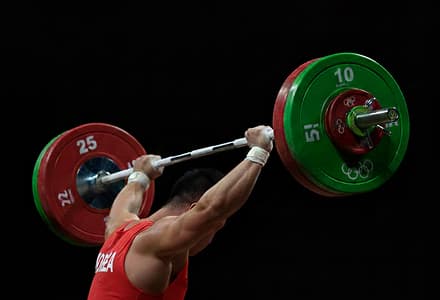 Korean weightlifter hoisting a loaded barbell overhead.