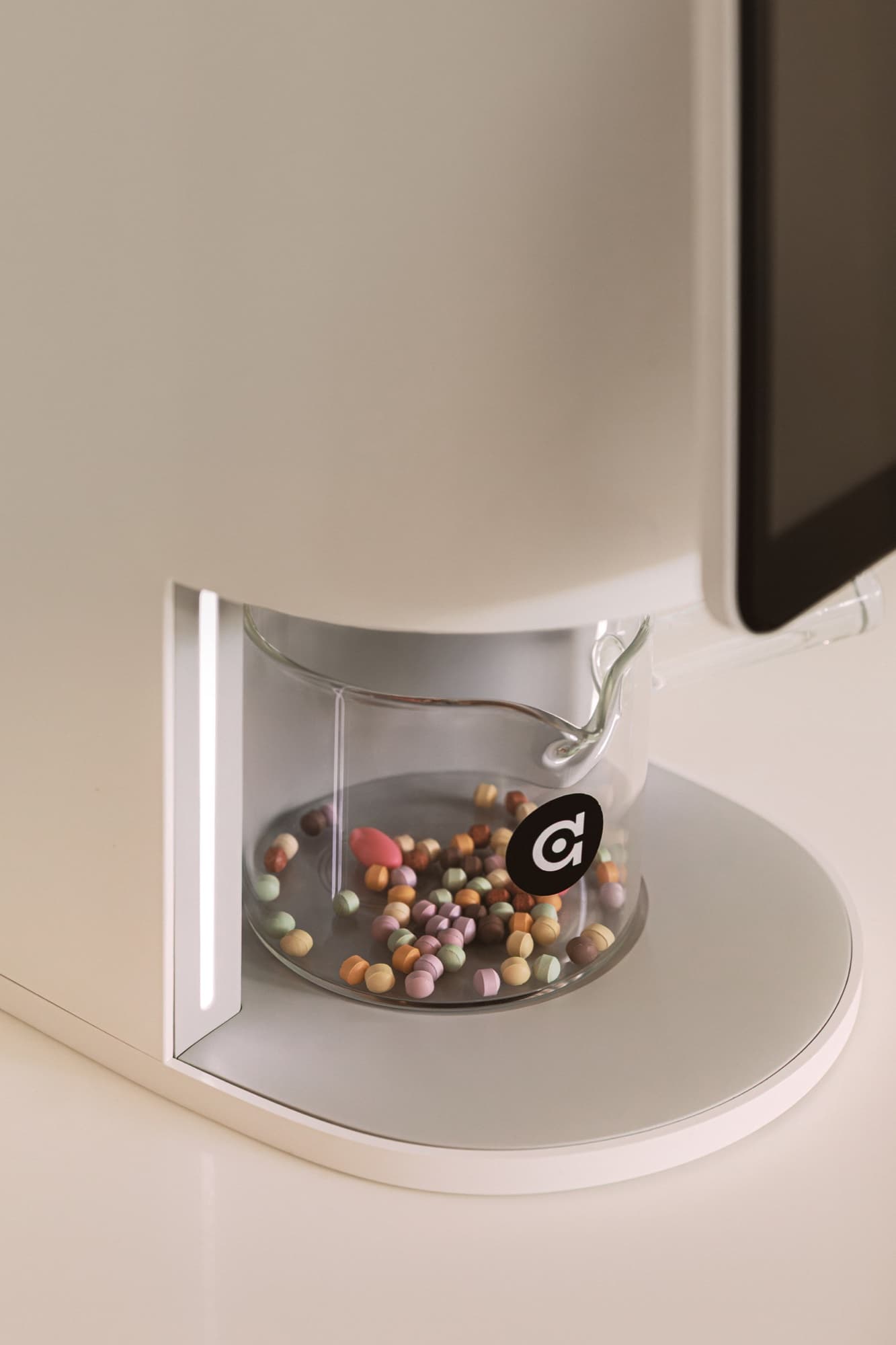 Close-up of the algocare E1 dispenser mid-dose, a single bead landing in a glass.